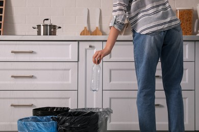 Woman throwing plastic bottle into trash bin in kitchen, closeup. Separate waste collection