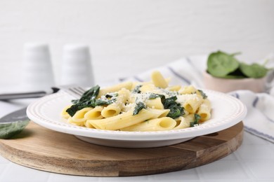 Tasty pasta with spinach and cheese on white tiled table, closeup