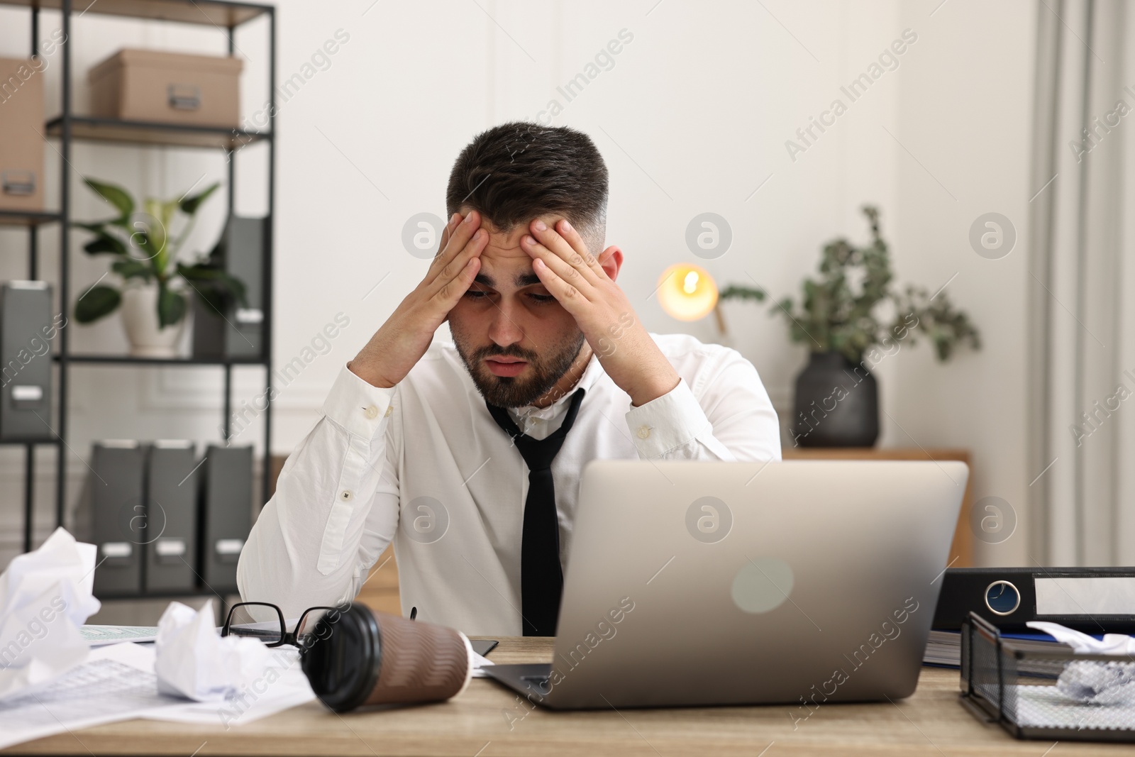 Photo of Overwhelmed man sitting at table with laptop and documents in office