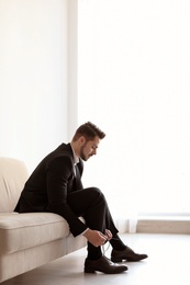 Photo of Young man putting on elegant leather shoes indoors