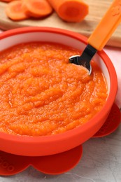 Photo of Healthy baby food. Bowl with delicious carrot puree on light grey marble table, closeup