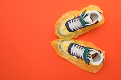 Sneakers in shoe covers on orange background, top view. Space for text