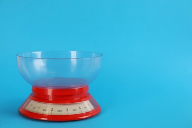 Photo of Kitchen scale with plastic bowl on light blue background, space for text