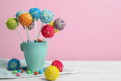 Photo of Cup with tasty cake pops on white table against pink background, space for text