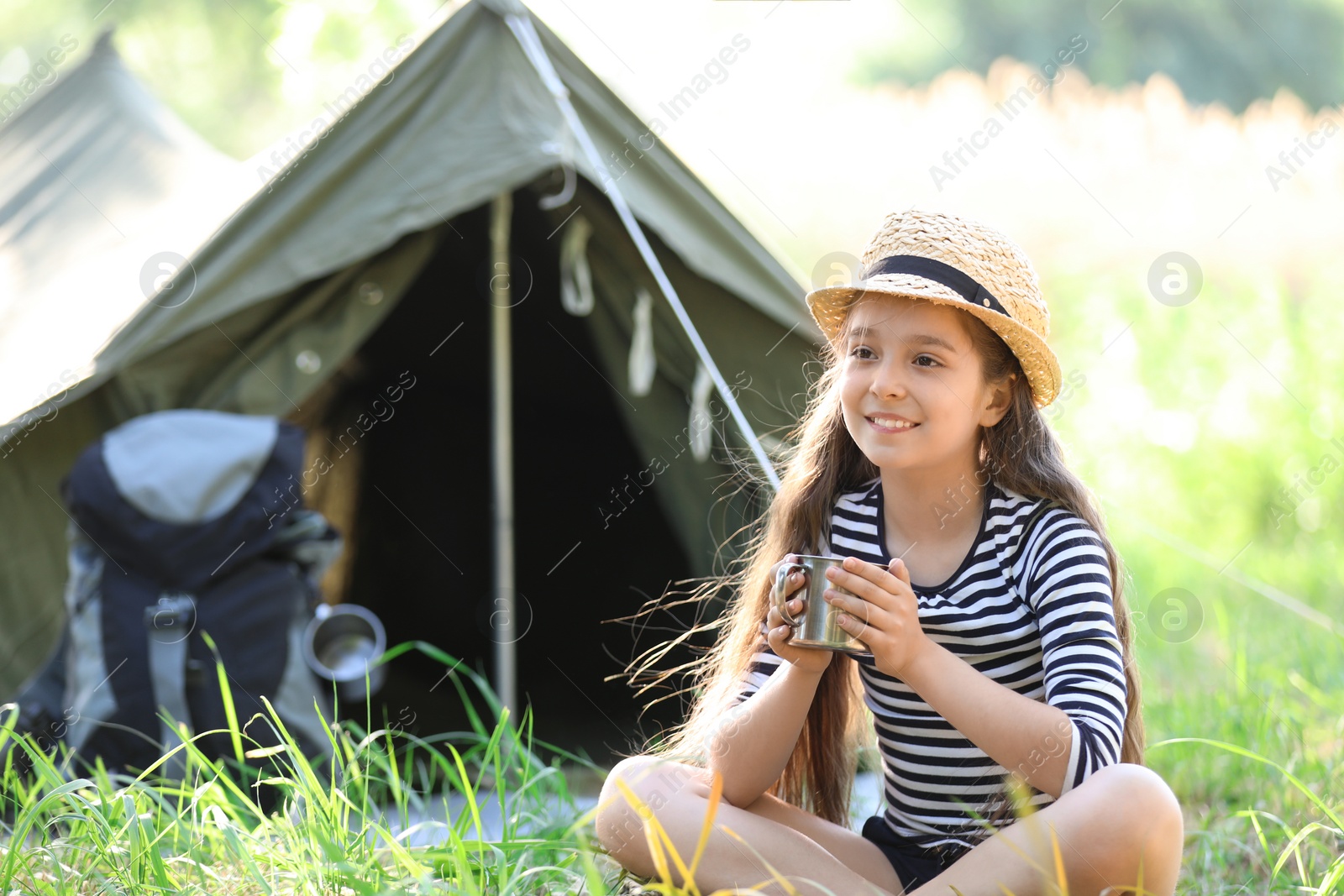 Photo of Little girl with mug near tent outdoors. Summer camp