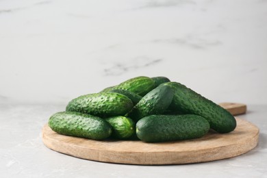 Photo of Board with fresh ripe cucumbers on white marble table, space for text