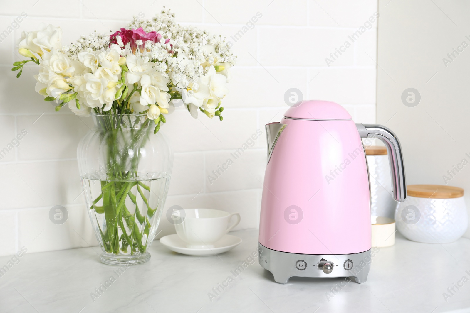 Photo of Modern electric kettle, cup and bouquet on counter in kitchen