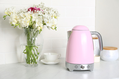 Photo of Modern electric kettle, cup and bouquet on counter in kitchen