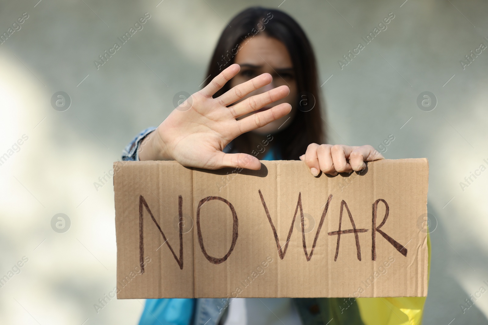 Photo of Young woman holding poster with words No War and showing stop gesture near light wall, focus on hand