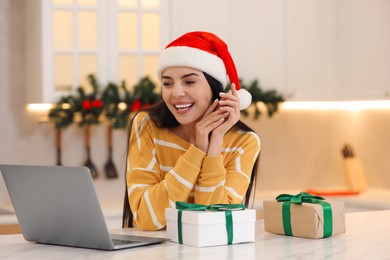 Photo of Celebrating Christmas online with exchanged by mail presents. Smiling woman with gift box during video call on laptop at home