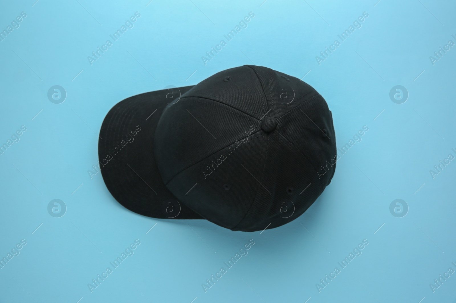 Photo of Stylish black baseball cap on light blue background, top view