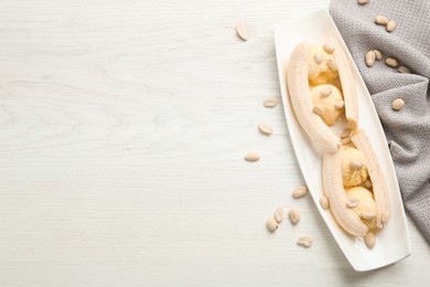 Delicious banana split ice cream portions and peanuts on white wooden table, flat lay. Space for text