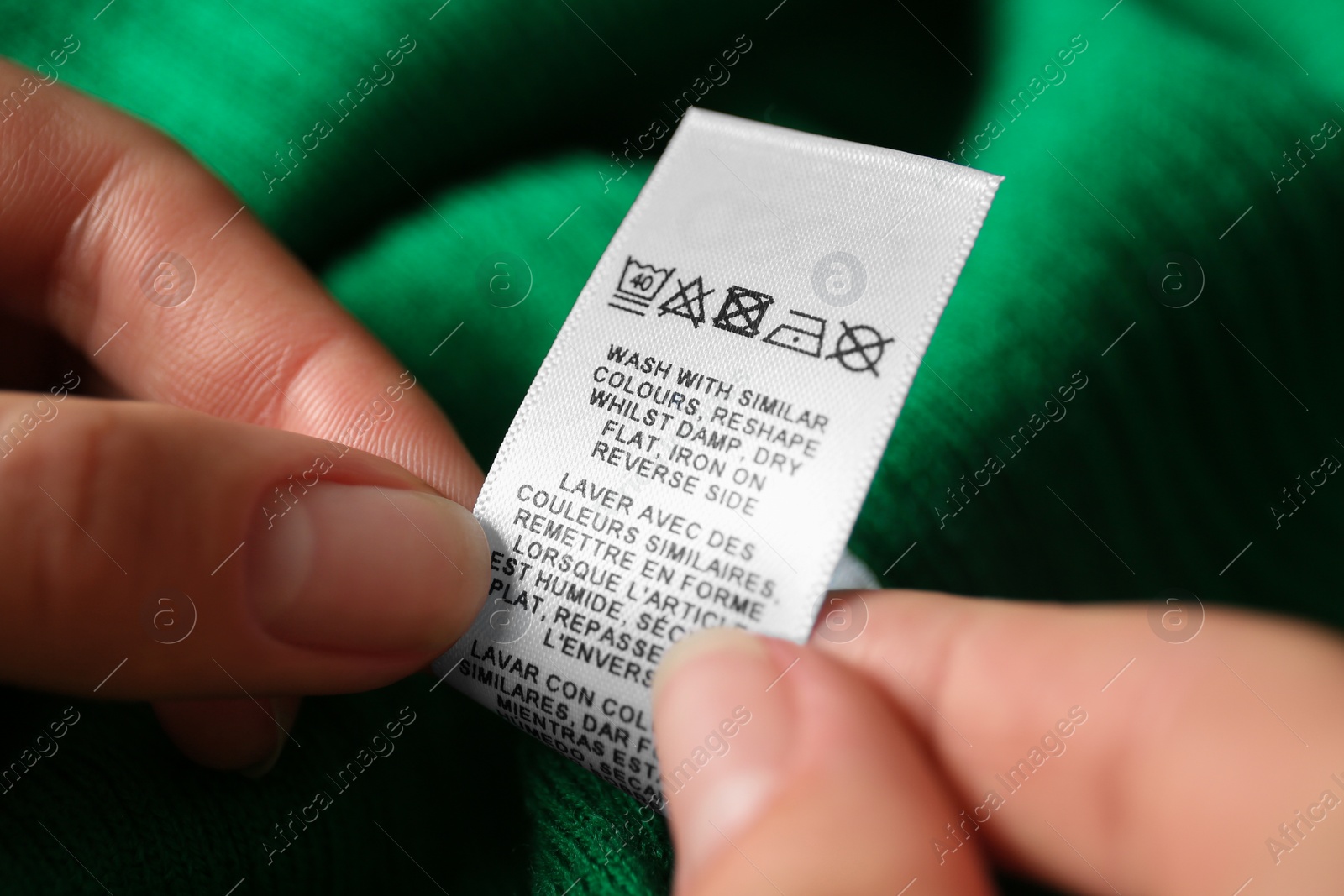 Photo of Woman reading clothing label with care symbols on green shirt, closeup