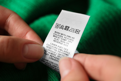 Photo of Woman reading clothing label with care symbols on green shirt, closeup
