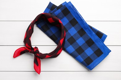 Photo of Tied and folded checkered bandanas on white wooden table, flat lay