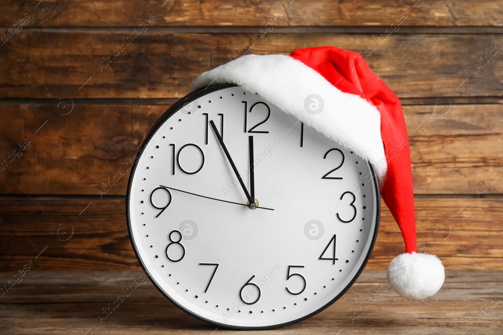 Photo of Clock with Santa hat showing five minutes until midnight on wooden background. New Year countdown