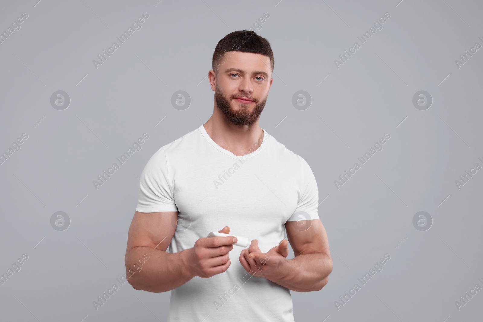 Photo of Handsome man applying body cream on light grey background