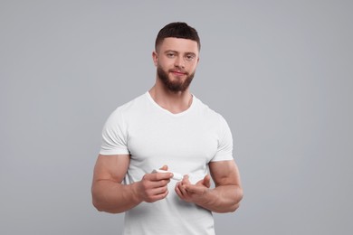 Handsome man applying body cream on light grey background