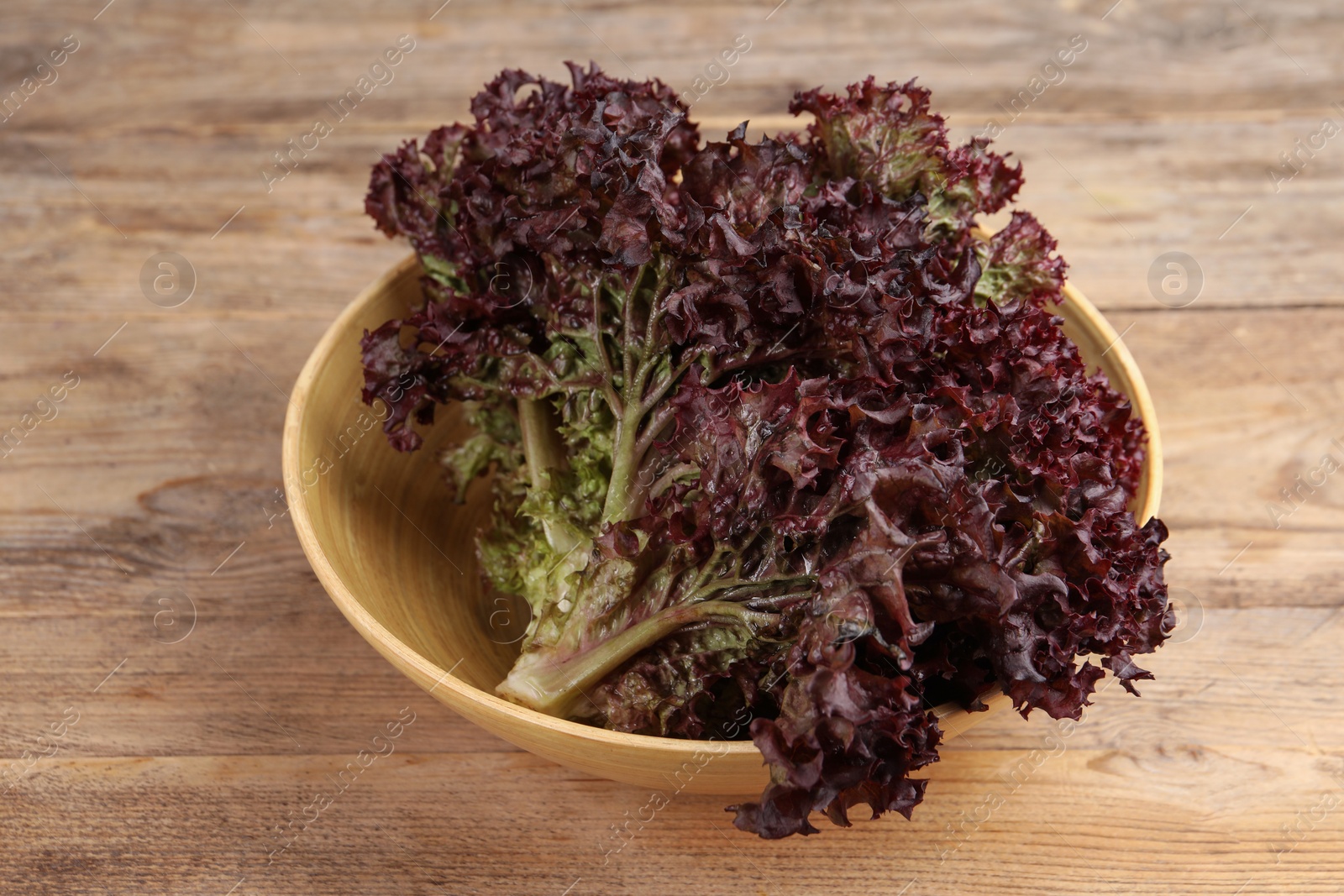 Photo of Bowl with fresh red coral lettuce on wooden table