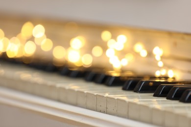 Photo of Glowing fairy lights on piano keys, closeup. Christmas music