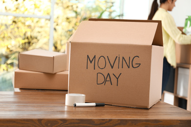 Photo of Cardboard box with words MOVING DAY and packaging items on wooden table