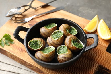 Delicious cooked snails in baking dish served on grey table, closeup
