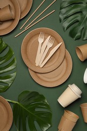 Flat lay composition with disposable tableware and monstera leaves on dark green background