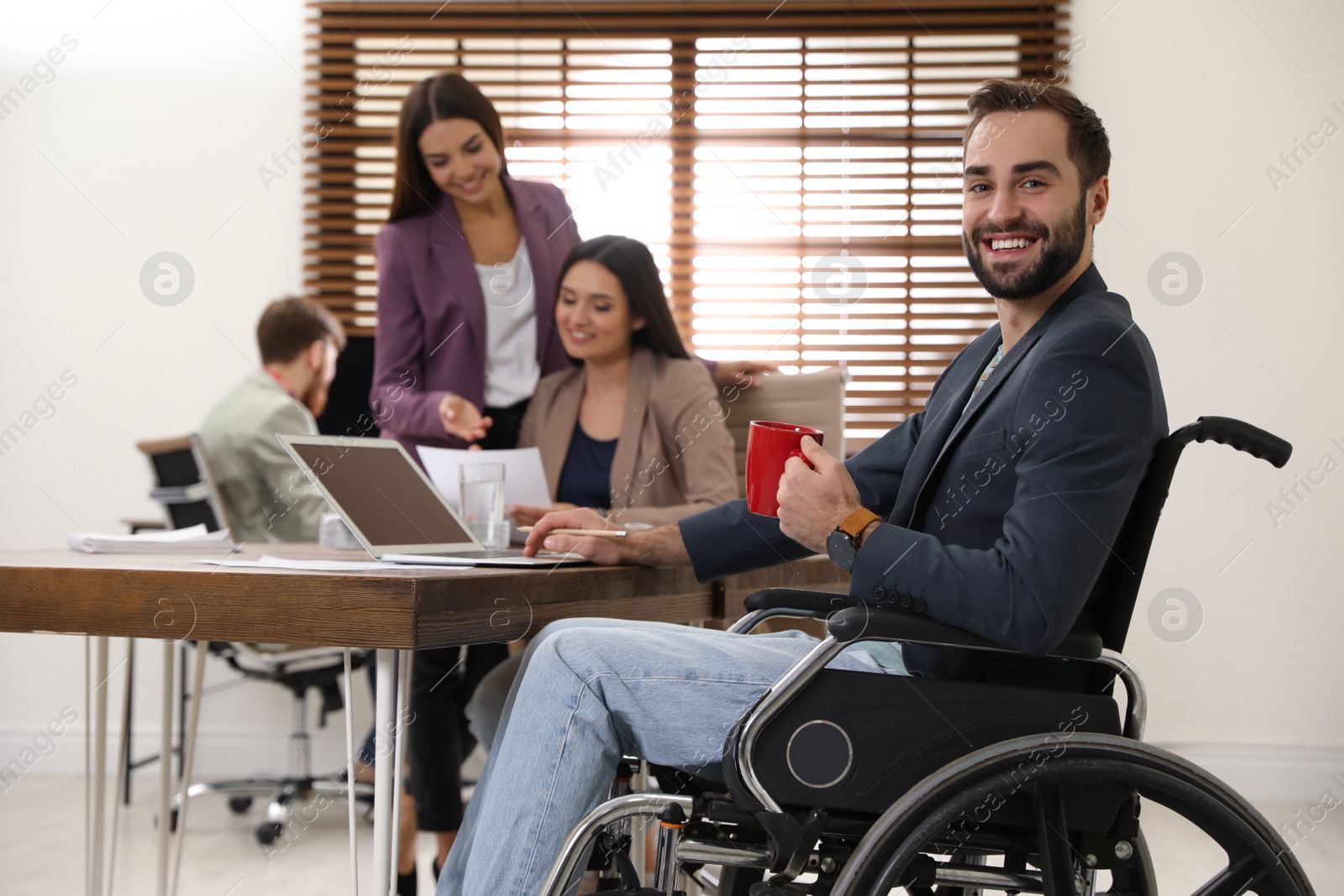 Photo of Young man in wheelchair with colleagues at workplace