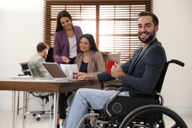 Photo of Young man in wheelchair with colleagues at workplace