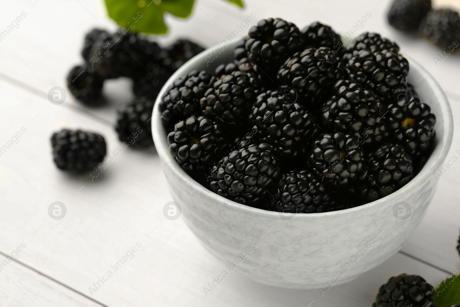Photo of Bowl with fresh ripe blackberries on white wooden table, closeup