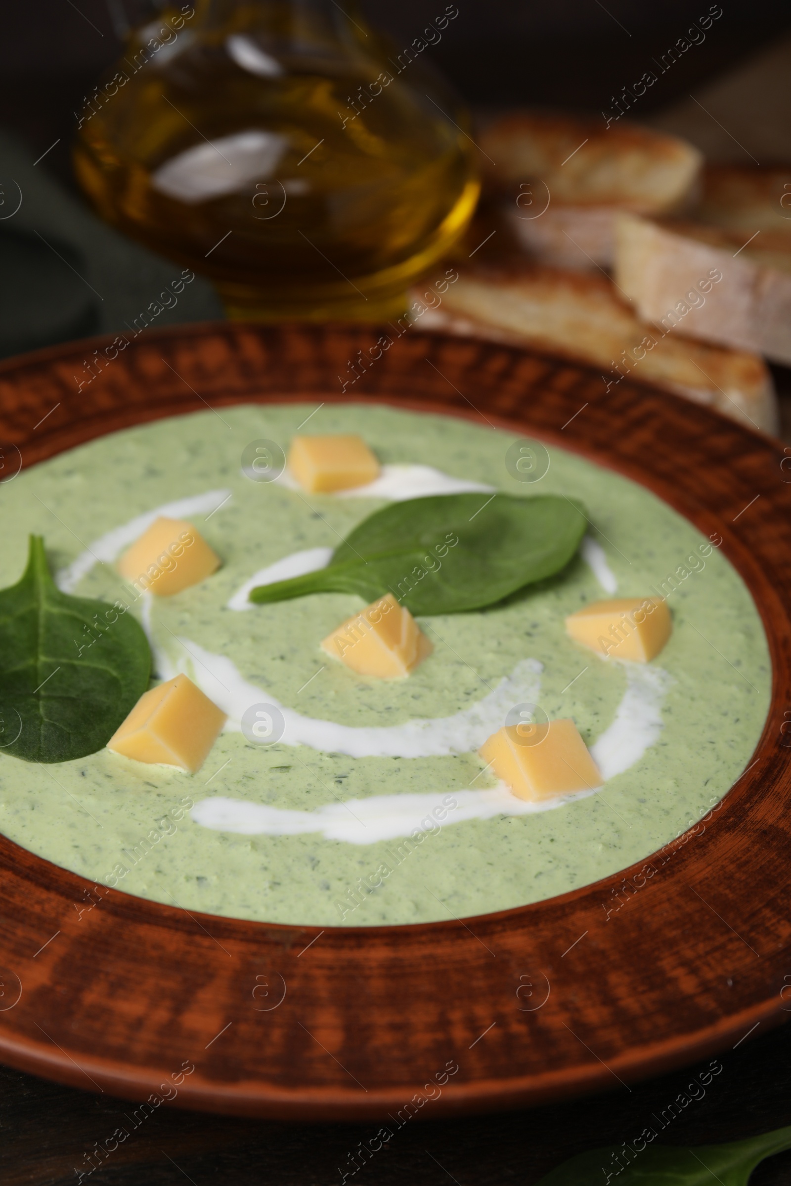 Photo of Delicious spinach cream soup with leaves and cheese in bowl on wooden table, closeup