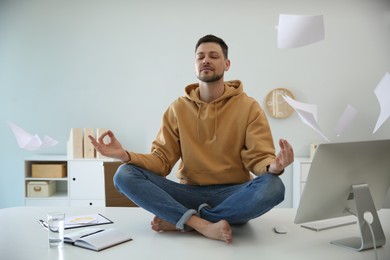 Photo of Calm man meditating on office desk in middle of busy work day