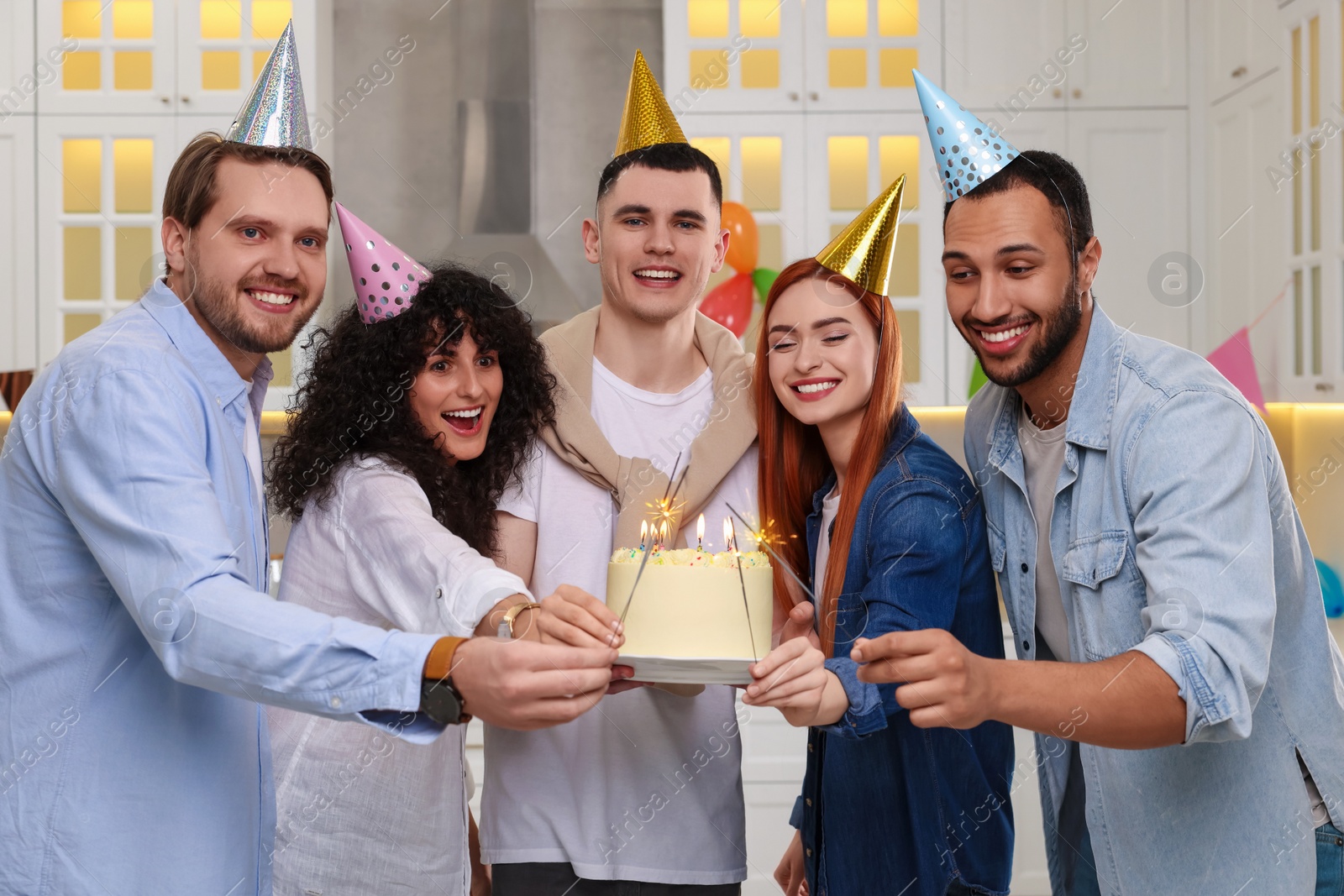 Photo of Happy friends with tasty cake and sparklers celebrating birthday in kitchen