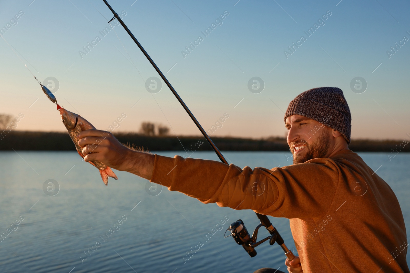 Photo of Fisherman with rod and caught fish at riverside