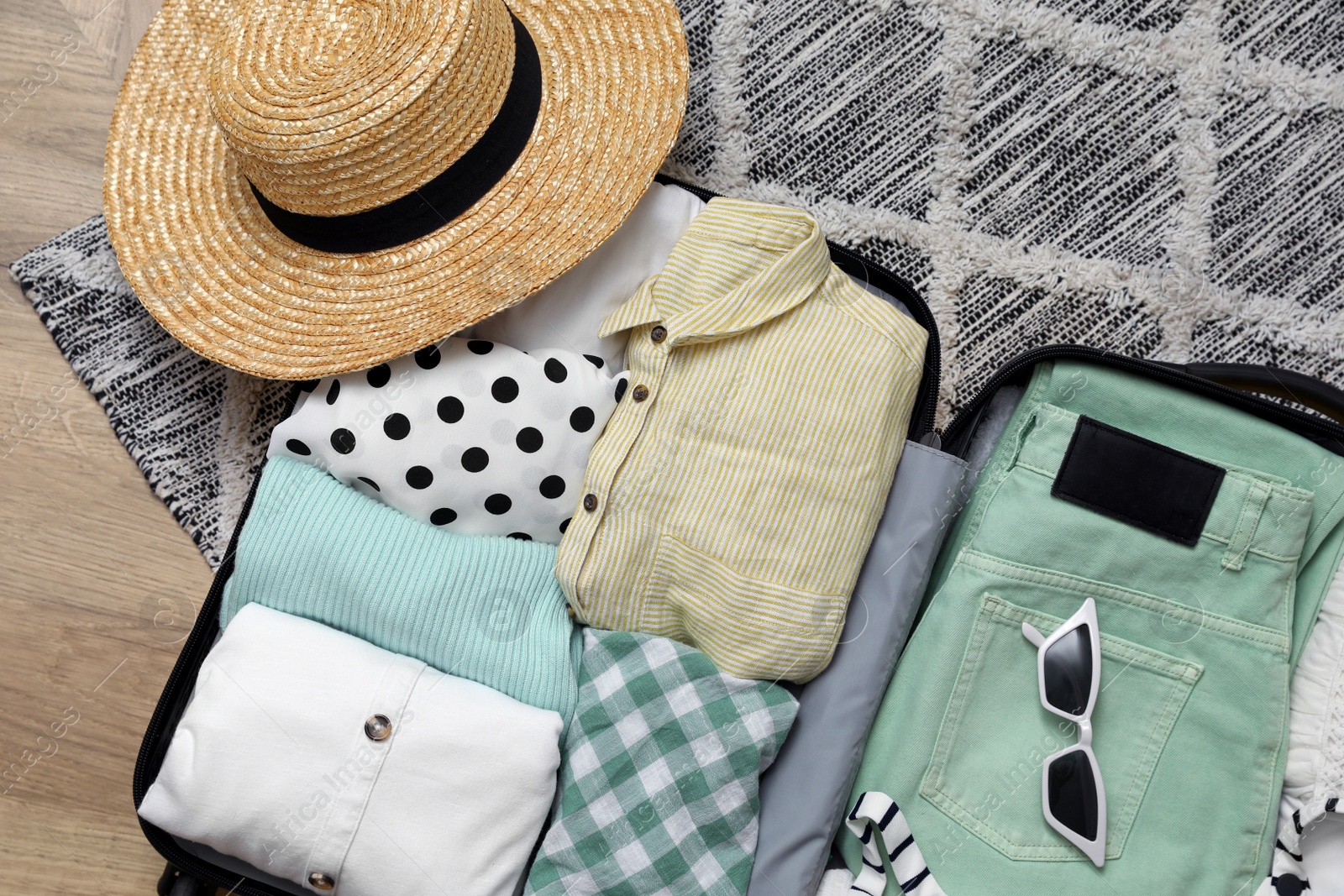 Photo of Open suitcase with summer clothes and accessories on floor, flat lay