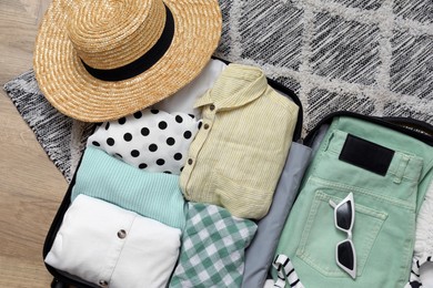 Open suitcase with summer clothes and accessories on floor, flat lay