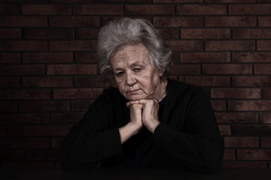 Photo of Poor upset woman sitting at table near brick wall
