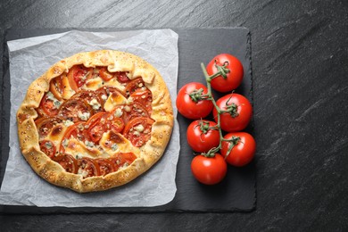 Photo of Tasty galette with tomato and cheese (Caprese galette) on dark textured table, top view. Space for text