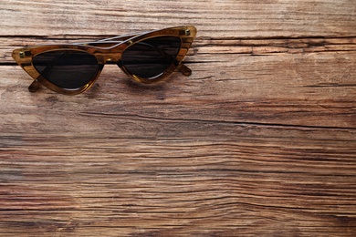 Photo of Stylish sunglasses on wooden background, top view. Space for text