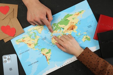 Man and woman planning their honeymoon trip with world map at black table, top view