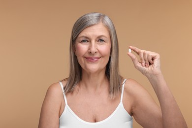 Photo of Beautiful woman with vitamin pill on beige background