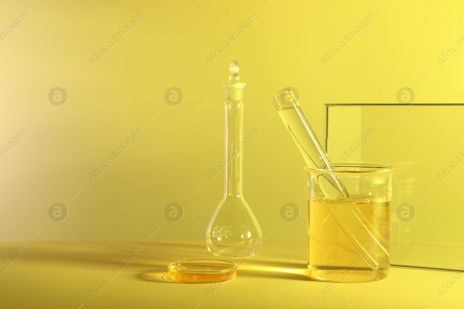 Photo of Laboratory analysis. Different glassware on table against yellow background, space for text