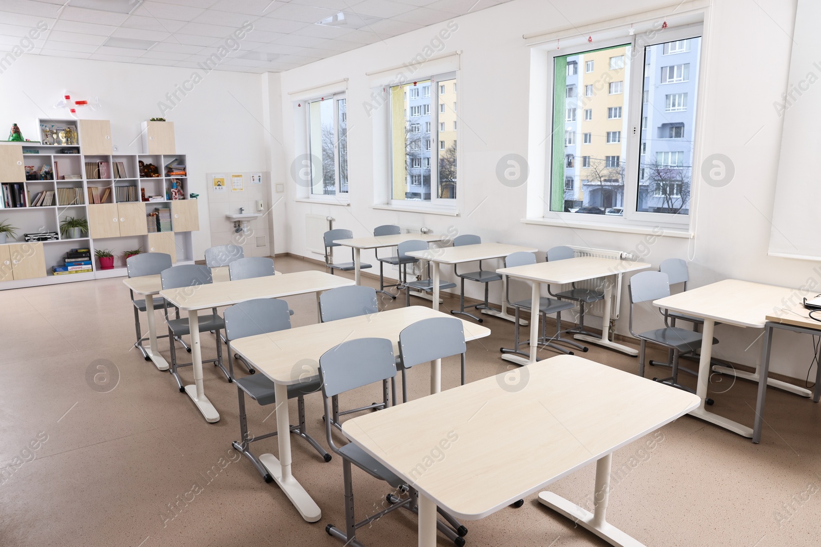 Photo of Empty school classroom with contemporary furniture and windows