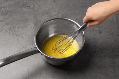 Photo of Woman whipping melting butter in saucepan on grey table, closeup