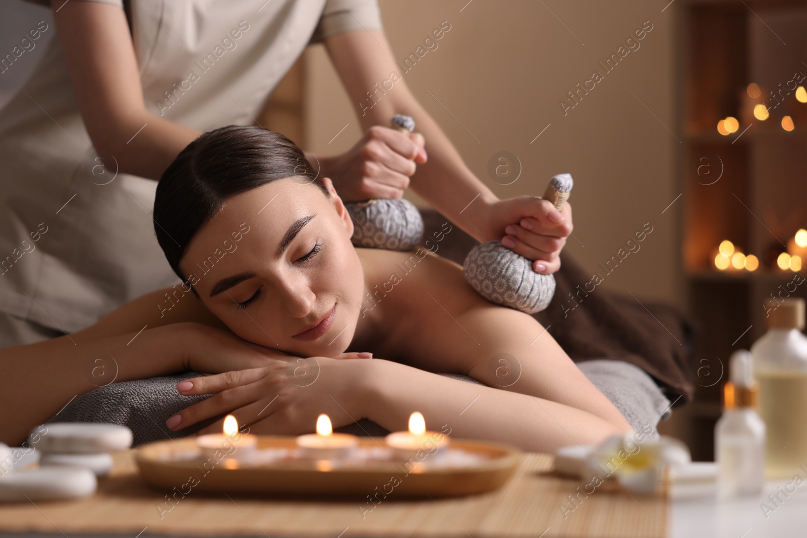 Photo of Spa therapy. Beautiful young woman lying on table during herbal bag massage in salon