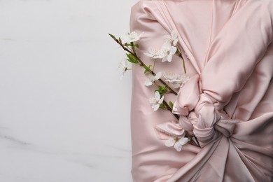 Furoshiki technique. Gift packed in pink fabric and beautiful flowers on white marble table, top view. Space for text