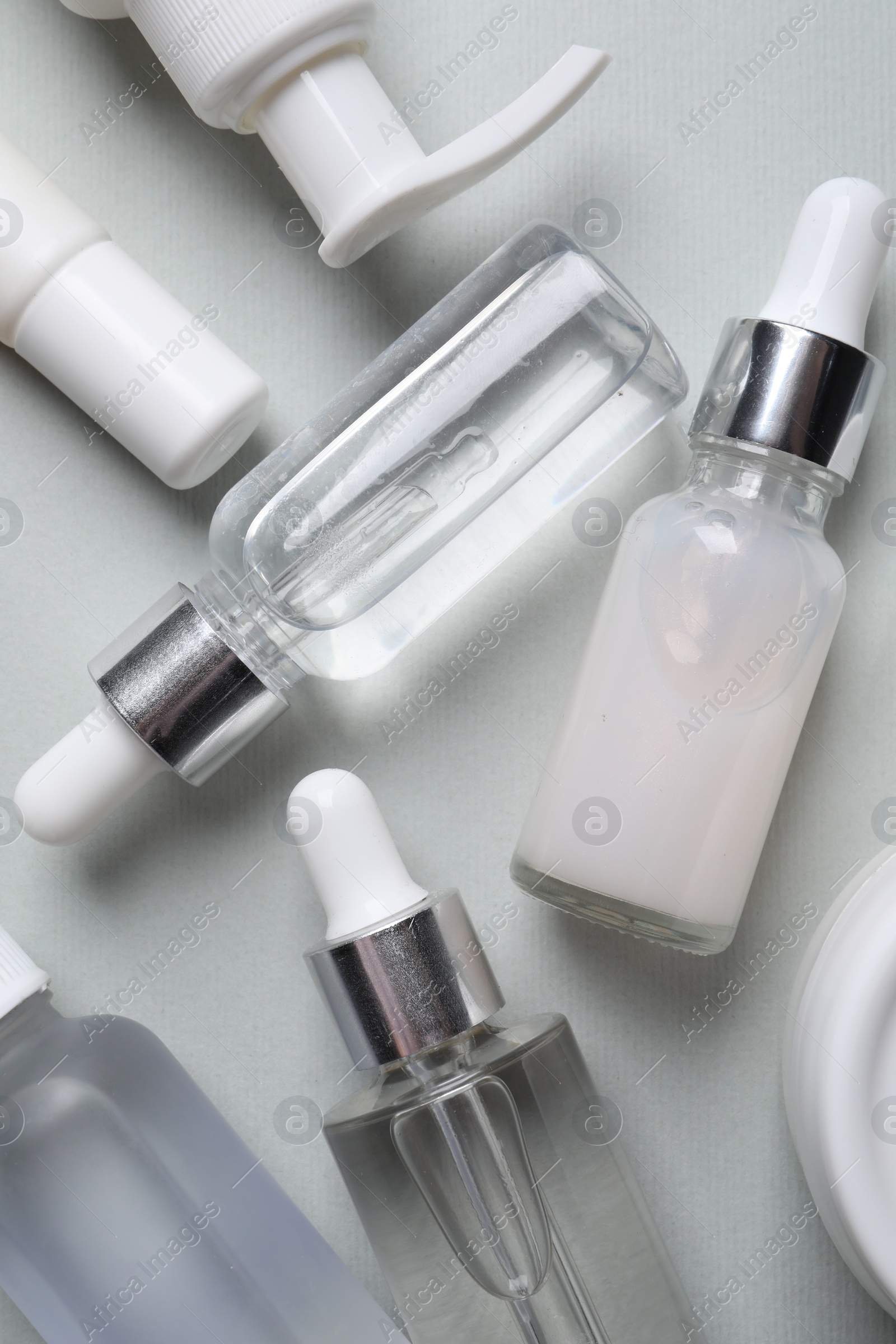 Photo of Many bottles of cosmetic serum on light grey background, flat lay