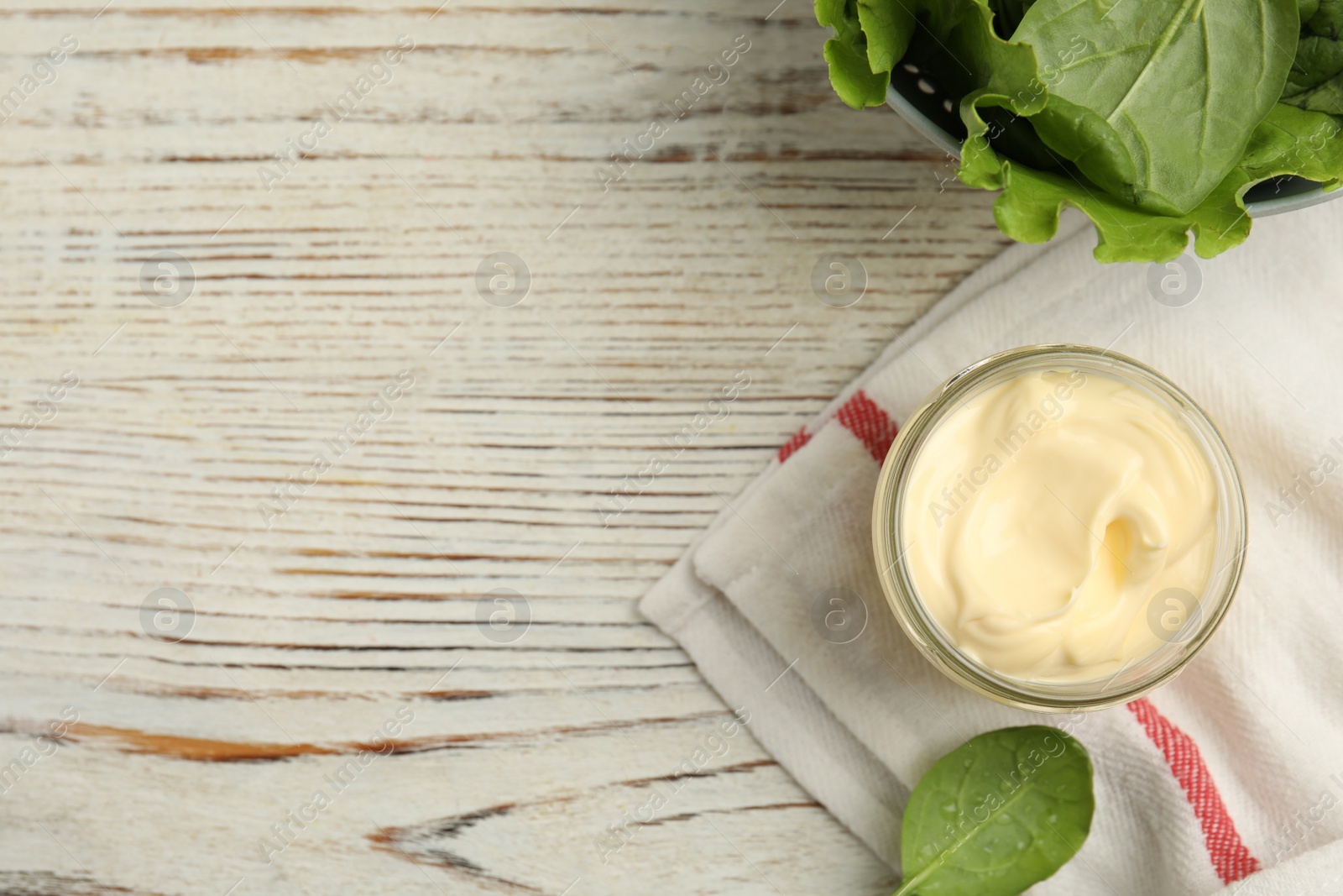 Photo of Jar of delicious mayonnaise and fresh spinach on white wooden table, flat lay. Space for text