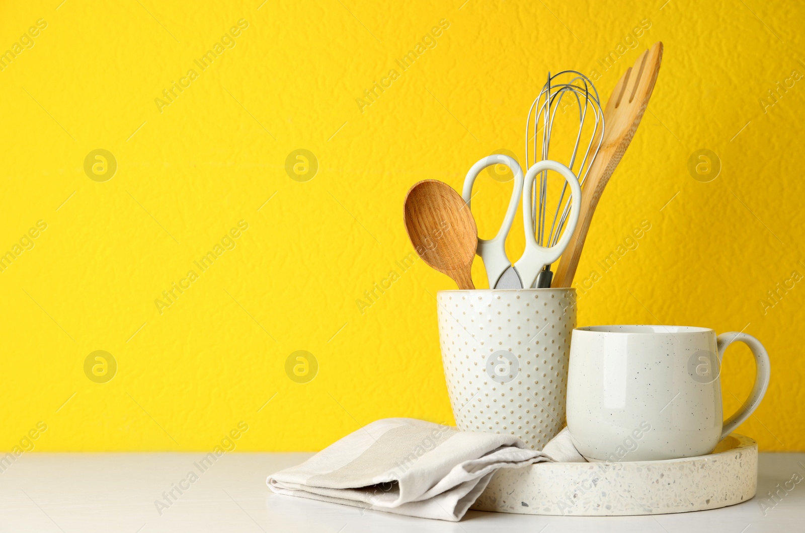 Photo of Different kitchen utensils on white table against yellow background. Space for text