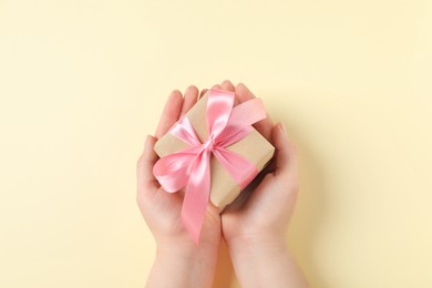 Woman with gift box on beige background, top view